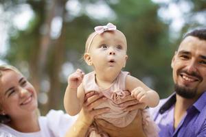 Ehemann, Ehefrau und ihr wenig Tochter zum ein gehen im das Park. glücklich Papa und Mama mit einer Jahr alt Baby Mädchen. jung Familie. foto