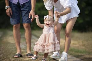 glücklich ein Jahr alt Mädchen ist Sein gehaltenen durch Papa und Mama. wenig Kind Gehen mit Eltern. ein süß Baby lernt zu gehen mit das Hilfe von ihr Eltern. foto