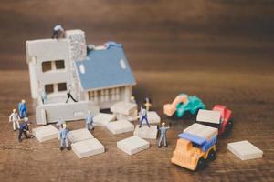 Miniaturarbeiter, die ein Haus auf einem hölzernen Hintergrund reparieren foto