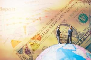 Miniaturgeschäftsleute, die auf einer Globus-Weltkarte mit einem Diagramm und Banknoten im Hintergrund stehen
