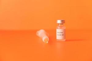 Nahaufnahme des Coronavirus-Impfstoffs und der Spritze auf orangefarbenem Hintergrund