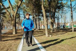 ein Alten aktiv Frau Spaziergänge im das Park auf skandinavisch Stöcke. gesund Lebensstil von Erwachsene Frauen. foto