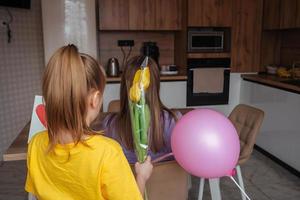 Tochter gratuliert Mama auf Mutter Tag, Karte mit Herz und Blumen. ein Frau sitzt beim ein Tabelle im das Küche und hat Frühstück mit ihr zurück zu uns. foto