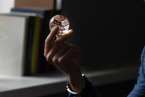 ein des Mannes Hand gegen das Hintergrund von ein Fenster im das Zimmer hält ein Kristall Glas Ball, suchen zum Antworten zu Fragen, Meditation foto