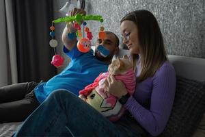 ein jung Paar auf das Bett Umarmungen ihr Katze eingewickelt im ein Baby Decke und Theaterstücke mit ihr mit ein Baby Rassel. bewusst Ablehnung von ein Paar zu haben Kinder, Behandlung von Haustiere wie Kinder. foto