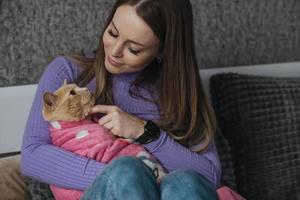 ein jung Frau im ihr Schlafzimmer hält ihr Haustier Katze eingewickelt im ein Baby Decke im ihr Waffen. Liebe und Pflege zum Tiere, kinderlos Frau. Behandlung Tiere mögen Ihre Kinder foto