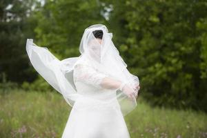 das Fett Braut versteckte im ein Hochzeit Schleier gegen das Hintergrund von Natur. foto