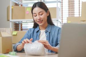 klein Geschäft Unternehmer klein, asiatisch jung Frau Inhaber Verpackung Produkt, Überprüfung Paket Box Lieferung, mit Laptop erhalten bestellen von Kunde, Arbeiten beim Zuhause Büro. Händler online, E-Commerce. foto