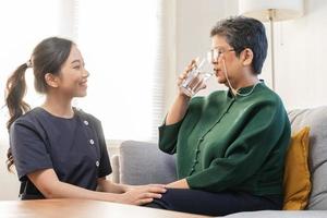 asiatisch jung Frau Betreuer, Pfleger unterstützen Alten, alt geduldig beim heim, Trinken Wasser nach nehmen Medizin, heilen oder Behandlung Krankheit von Oma nach Ruhestand, Hilfe Unterstützung. foto