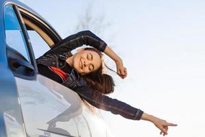 glücklich Frau winken ihr Hand auf ein öffnen gefenstert Auto gegen Blau Himmel und Sonne. foto