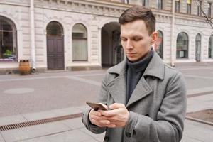 Mann im grau Mantel und Sweatshirt steht auf Stadt Straße. Gespräche auf Telefon. löst foto