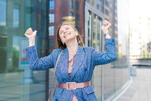 glücklich Geschäft Frau zeigen Daumen oben während Stehen draußen gegen Büro foto