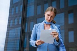 Geschäftsfrau hält Unterlagen ihr Hand gegen Hintergrund von ein Büro Gebäude foto