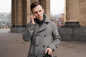 Mann im grau Mantel und Sweatshirt steht auf Stadt Straße. Gespräche auf Telefon. löst foto