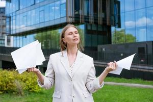 schön jung Vorort- Geschäft Frau Gehen im klassisch städtisch Büro Gebäude halten Papier Unterlagen und lächelnd foto