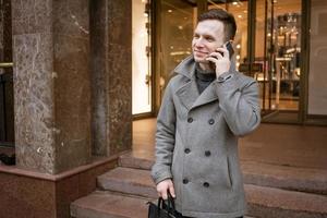 Mann im grau Mantel und Sweatshirt steht auf Stadt Straße. Gespräche auf Telefon. löst foto