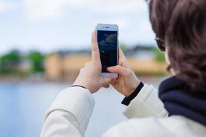 jung Frau auf Ferien mit Handy, Mobiltelefon Telefon zu nehmen Bilder Fluss und Stadt foto