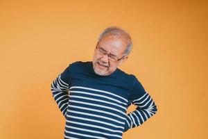 asiatisch Senior Mann Gefühl Rückenschmerzen oder zurück Schmerzen auf das Gelb Hintergrund. foto