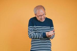 asiatisch Senior Mann Gefühl Handgelenk Schmerzen auf das Gelb Hintergrund. foto
