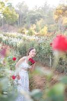 jung asiatisch Frau tragen ein Weiß Kleid posiert mit ein Rose im Rose Garten foto