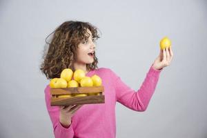 Porträt einer jungen lockigen Frau, die eine Schachtel mit frischen Zitronen hält foto