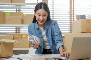 klein Geschäft Unternehmer klein, asiatisch jung Frau Inhaber Verpackung Produkt, Überprüfung Paket Box Lieferung, mit Laptop erhalten bestellen von Kunde, Arbeiten beim Zuhause Büro. Händler online, E-Commerce. foto