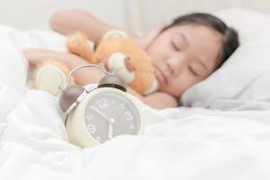 Alarm Uhr auf Bett und Mädchen Schlaf auf Hintergrund foto