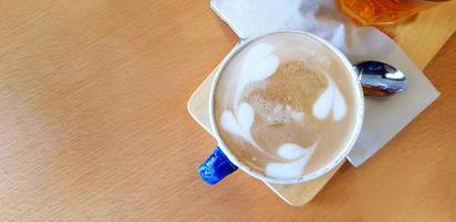 oben Aussicht Tasse von heiß Latté Kunst im Herz oder Blätter Stil mit Tee Löffel und Glas von Wasser auf braun hölzern Tabelle mit links Kopieren Raum. Erfrischung Trinken und Essen Design Konzept foto