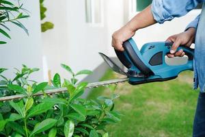 Gärtner trimmt Busch mit elektrischen Heckenscheren im Garten. Hobby zu Hause. foto