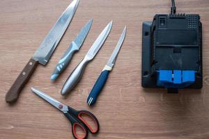 Schärfung ein Messer auf ein elektrisch Anspitzer beim heim. Flatlay Messer Klinge, Schere, Spitzer, Staub fliegt auf das Maschine. foto