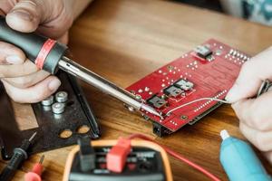 Techniker Mann halten Eisen löten und reparieren das Schaltkreis Tafel durch Löten. elektrisch Arbeit Konzept foto