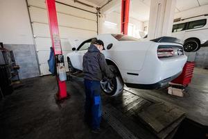 Mechaniker in Service-Reparaturstation, der mit Muscle-Car im Aufzug arbeitet. foto