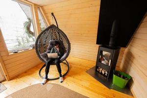 Teenager Junge sitzen mit Laptop Innerhalb Ei schwingen gegen Kamin beim gemütlich drinnen Heizung. foto