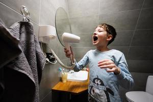 Junge Singen mit ein Haar Trockner beim Badezimmer. foto