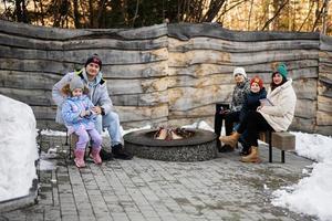 Familie mit drei Kinder Sitzung durch Lager Lagerfeuer auf Winter im Wald. Kinder im Landschaft. foto