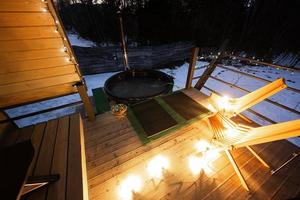 hölzern Fass heiß Wanne im das Terrasse von das Hütte beim Winter Nacht. skandinavisch Badewanne mit ein Kamin zu brennen Holz und Hitze Wasser. foto