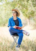 Frau trägt Hut und liest das Buch auf dem Stuhl foto