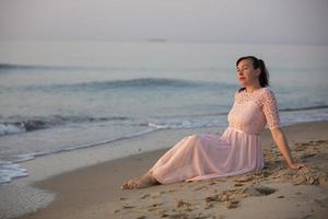 ein schön mittleren Alters Frau im ein Kleid sitzt durch das Strand. foto