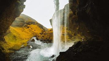 weiblich Tourist gehen auf Weg Besuch berühmt kvernufoos Wasserfall Wahrzeichen. Gelb Gras Hügel auf kvernufoss Wasserfall. majestätisch Sommer- Aussicht von rein Wasser Fluss im Island, Europa foto