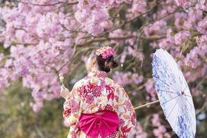 zurück von japanisch Frau im traditionell Kimono Kleid halten Regenschirm und Süss Hanami Dango Dessert während Gehen im das Park beim Kirsche blühen Baum während das Frühling Sakura Festival mit Kopieren Raum foto