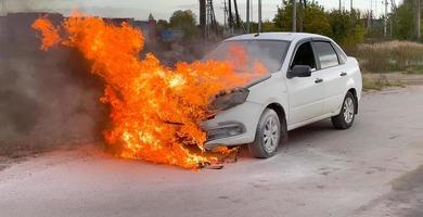 Unfall. ein Weiß Auto im ein industriell Bereich ist auf Feuer. das Motor Abteil ist auf Feuer foto