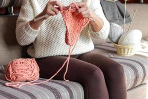 ein Frau sitzt auf ein Sofa im ein Zimmer und strickt ein Schal. Hobbys, Haushalt Hausarbeiten. foto