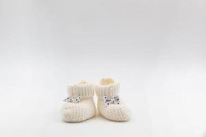 gestrickt Weiß Baby Booties mit Tupfen Bögen auf ein grau isoliert Hintergrund. Hintergrund. zum Text. Foto im hoch Qualität