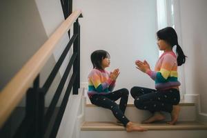 Geschwister asiatisch Mädchen spielen Felsen Papier Schere Hand Spiel. Kinder Sitzung auf Treppe beim Zuhause spielen zusammen. foto