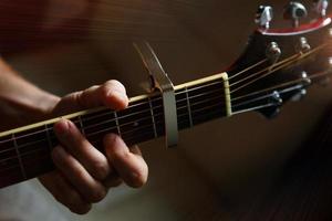 ein des Mannes Hand auf das Griffbrett von ein Gitarre läuft seine Finger durch das Saiten und Klemmen das Akkorde. instrumental Musik, Gitarre Lektion auf Blatt Musik- foto