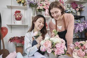 zwei junge schöne weibliche floristenpartner, die zusammen einen blumenstrauß arrangieren und dekorieren, lächeln mit glücklicher arbeit in einem farbenfrohen blumenladengeschäft mit frischen blüten, einem kleinen unternehmer.