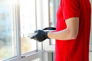 ein Mann Hände Gummi Handschuhe mit ein Box Pizza in der Nähe von das Fenster . Kurier. Essen Lieferung während das Quarantäne von das Coronavirus Pandemie. Ausgabe von Aufträge, online Befehl. foto