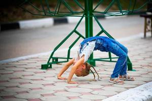 ein wenig Mädchen macht ein Brücke, Biegen ihr zurück im Straße . ein flexibel Kind, tun Gymnastik Übungen. foto