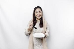 ein asiatisch Muslim Frau ist Fasten und hungrig und halten Utensilien Besteck während suchen beiseite Denken Über Was zu Essen foto