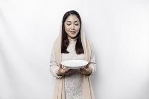 ein asiatisch Muslim Frau ist Fasten und hungrig und halten Utensilien Besteck während suchen beiseite Denken Über Was zu Essen foto